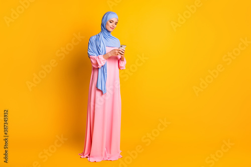 Full length body size view of nice lovely elegant focused muslimah wearing hijab using device app 5g isolated shine yellow color background