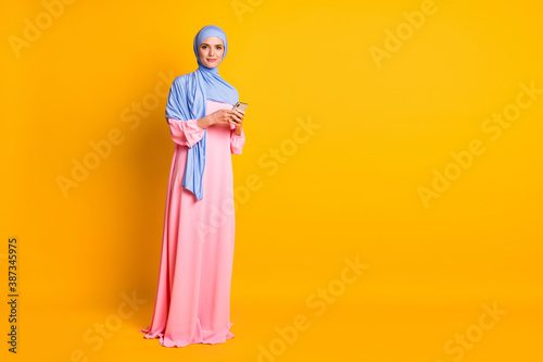 Full length body size view of nice pretty elegant muslimah wearing hijab dress using device blog isolated on bright yellow color background