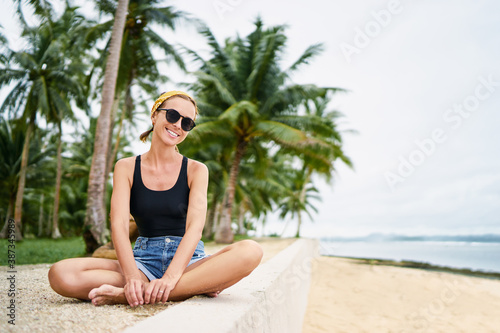 Vacation on the seashore.Young woman in shorts and sunglasses on the tropical beach with palm trees.