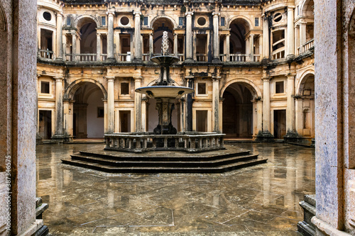 Entrance To Wet Reflective Courtyard With Fountain, Bordered By Cloister. Tomar, Portugal