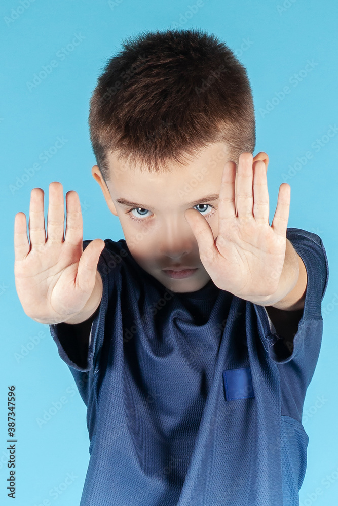 Close up portrait of pretty little Caucasian boy with blue eyes making stop gesture with both hands, seriously looking right to the camera. Cyan background. Concept of ban of children abuse. Close up portrait of pretty little Caucasian boy with blue eyes making stop gesture with both hands, seriously looking right to the camera. Cyan background. Concept of ban of children abuse.