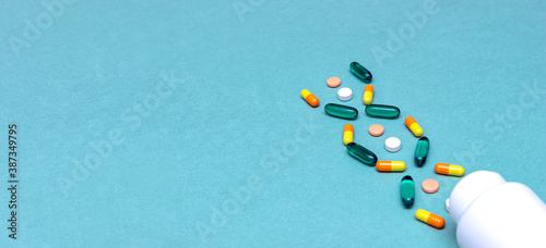 white, green, red and yelloy pills with white bottle on blue background. medical concept. concept of genetic illness photo