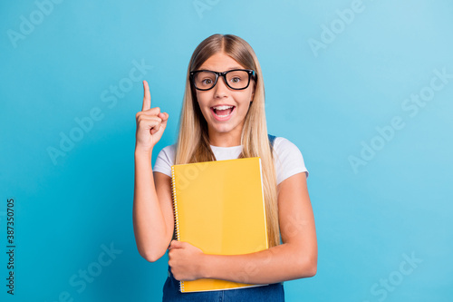 Photo of funny positive blond hair girl have idea pointing up wear spectacles hold book isolated on blue color background