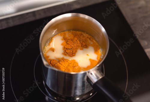 Curcuma dry powder in a pot with almond milk, making of turmeric latte.