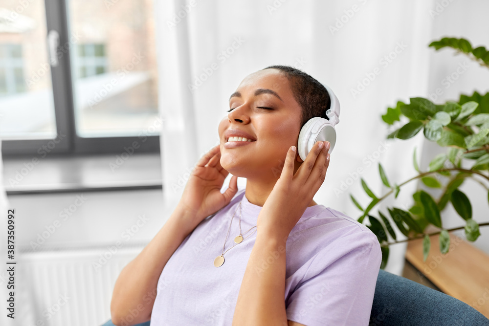 people, technology and leisure concept - happy young african american woman in headphones sitting in chair and listening to music at home people, technology and leisure concept - happy young african american woman in headphones sitting in chair and listening to music at home