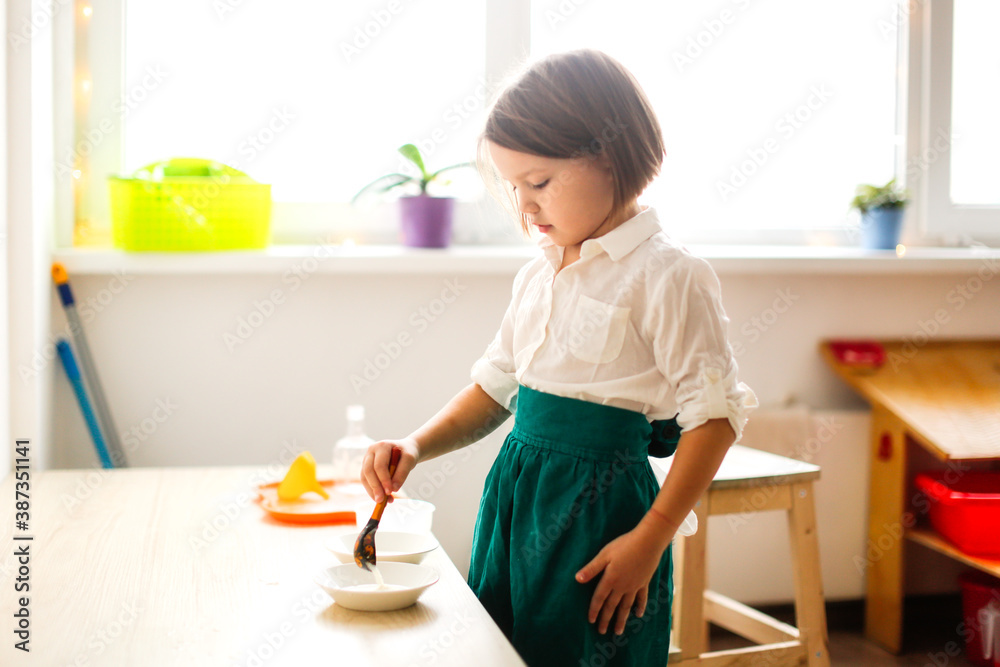 child girl in a linen apron plays with bulk cereals, developing sensory activities in montessori and earlier child development, children's independence
