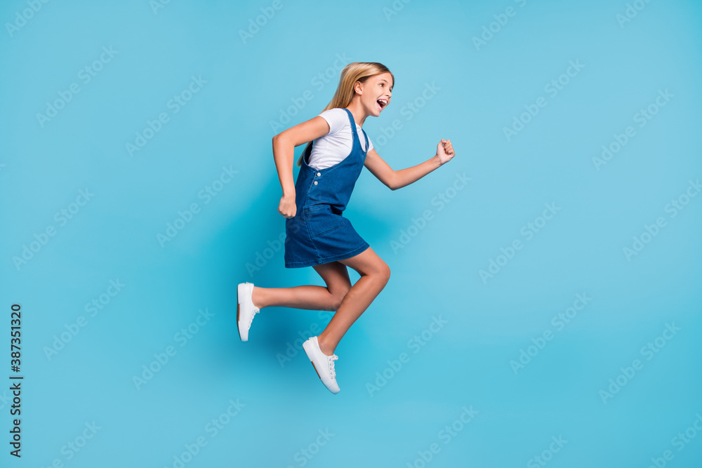 Profile full size photo of cheerful funny blond girl jumping yell wear t-shirt dress sneakers isolated on pastel blue color background
