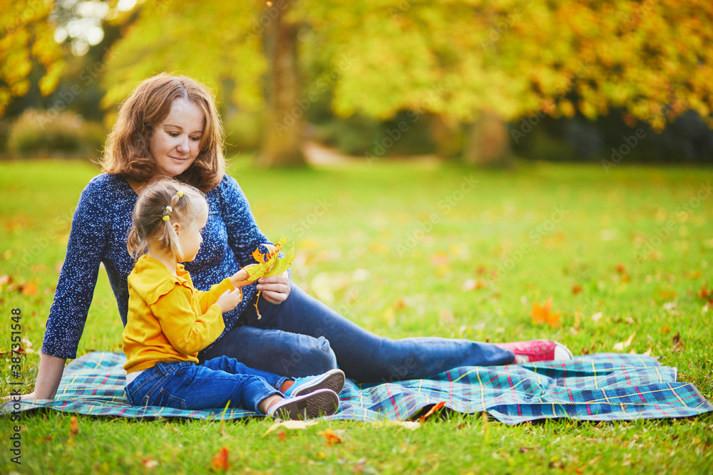 Woman and adorable toddler girl sitting on the ground and having picnic in autumn park Woman and adorable toddler girl sitting on the ground and having picnic in autumn park