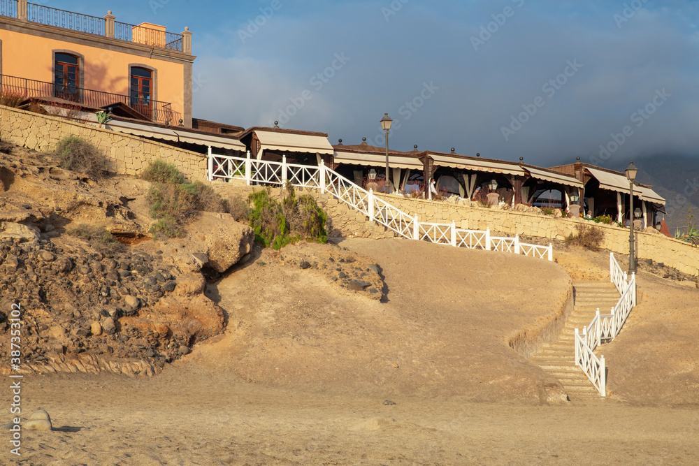 Obraz premium Wooden stairway path connecting the beach with the long promenade lined up with elegant restaurants, shops and entertainment, Playa del Duque, Adeje, Tenerife, Canary Islands, Spain