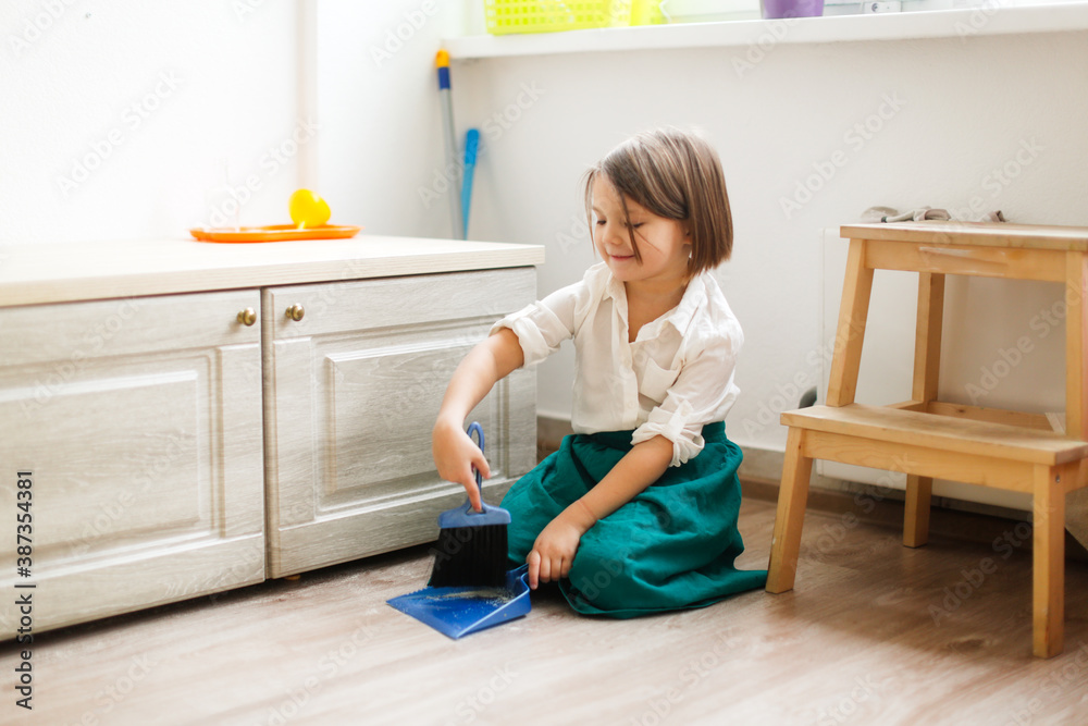 child girl in linen apron sweeps floor with brush and dustpan, developing sensory activities in Montessori and earlier child development, independence of children and helping mother child girl in linen apron sweeps floor with brush and dustpan, developing sensory activities in Montessori and earlier child development, independence of children and helping mother