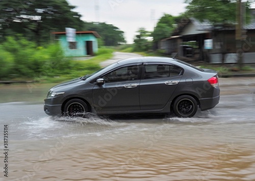 A black car is running on a road with water on the road.