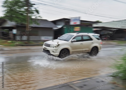 A white car is running on a road with water on the road.