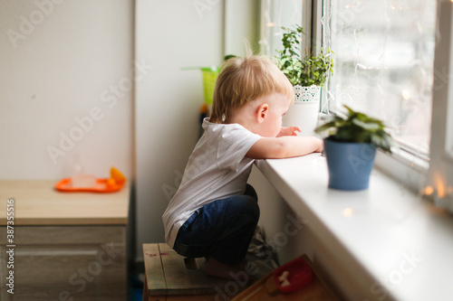 A lonely sad toddler toddler looks out the window with tears, a child in kindergarten without a mom, mom left home without a child