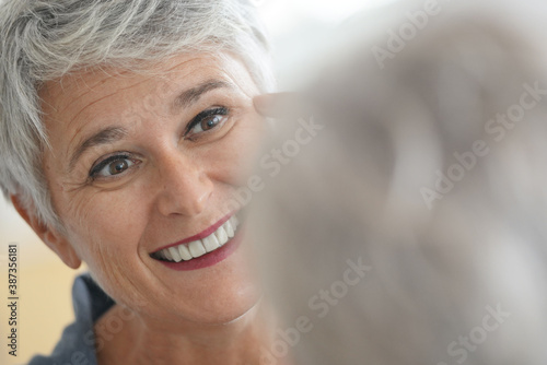 Mature white-haired woman checking eye wrinkles in front of mirror