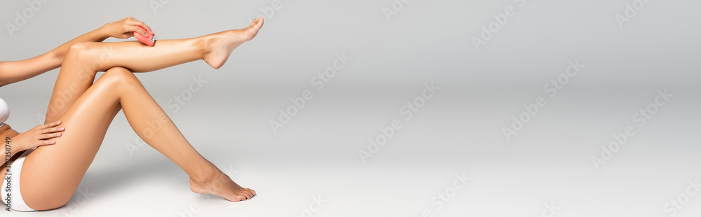Εκτύπωση καμβά Woman in white underwear shaving leg with epilator on grey, banner