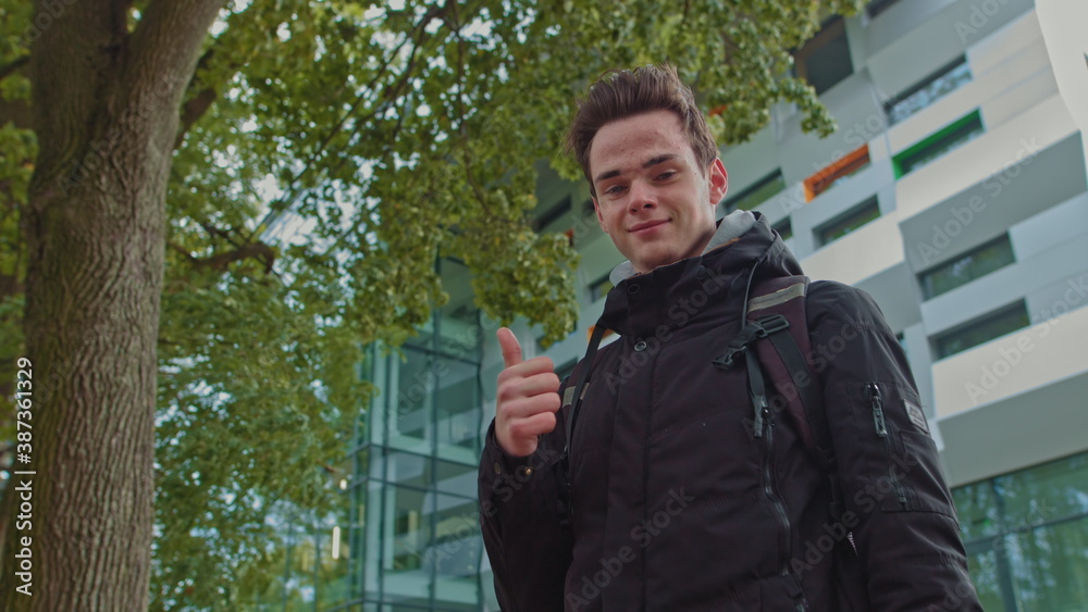 Handsome smiling young guy of 18 years in modern warm clothes on the background of the business center shows like. People sincere emotions, lifestyle concept. Looking approvingly at the camera showing Handsome smiling young guy of 18 years in modern warm clothes on the background of the business center shows like. People sincere emotions, lifestyle concept. Looking approvingly at the camera showing