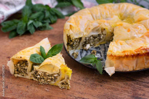 Spiral pie made of filo dough, spinach and feta cheese on wooden background. Authentic Greek bakery.