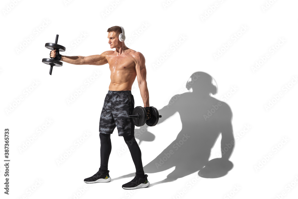 Dumbbells and weights. Stylish young male athlete on white studio background, portrait with shadows. Sportive fit model in motion and action. Body building, healthy lifestyle, style concept. Dumbbells and weights. Stylish young male athlete on white studio background, portrait with shadows. Sportive fit model in motion and action. Body building, healthy lifestyle, style concept.