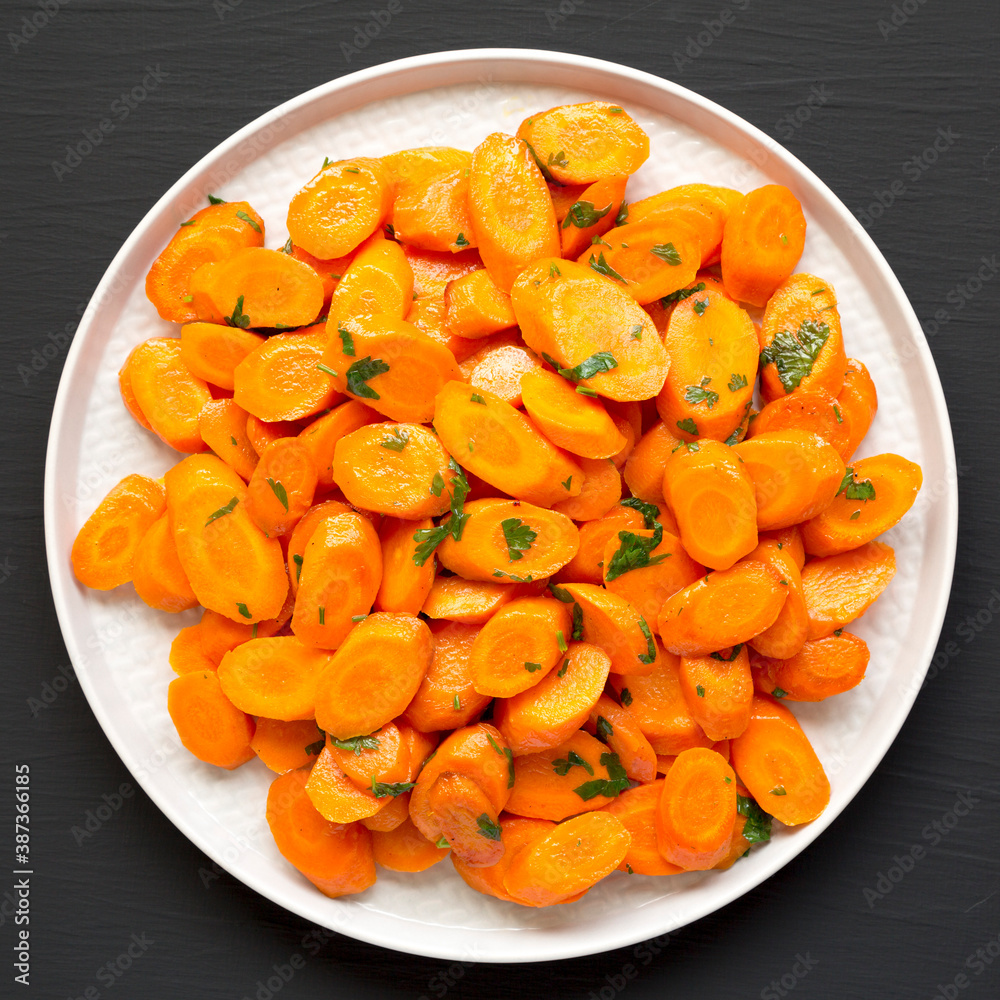 Homemade Sauteed Carrots on a plate on a black surface, top view. Flat lay, overhead, from above. Homemade Sauteed Carrots on a plate on a black surface, top view. Flat lay, overhead, from above.