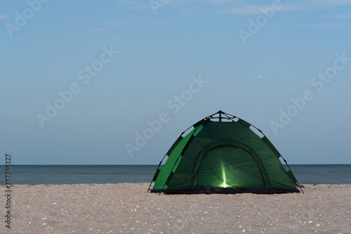 Camping tent on the seashore glowing from the inside. Evening