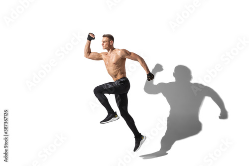 Running, jumping high. Stylish young male athlete on white studio background, portrait with shadows. Sportive fit model in motion and action. Body building, healthy lifestyle, style concept.