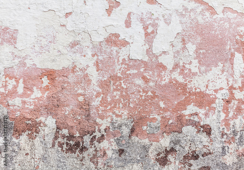 Close-up texture of a wall with a peeled peeling white fringe through which you can see the pink base