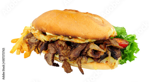 Steak and cheese sandwich with fried onions and French fries in a crusty bread roll isolated on a white background