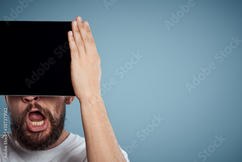 man with touch tablet in front of face on blue background cropped view copy space emotions model