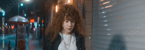Young woman with curly hair in white t-shirt and black jacket is walking on the street at night, fashion clothing and feminism concept