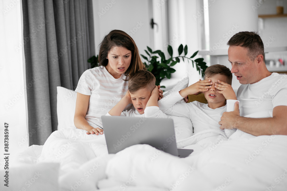 Beautiful parents with kids enjoying at home. Young family watching movie on lap top.