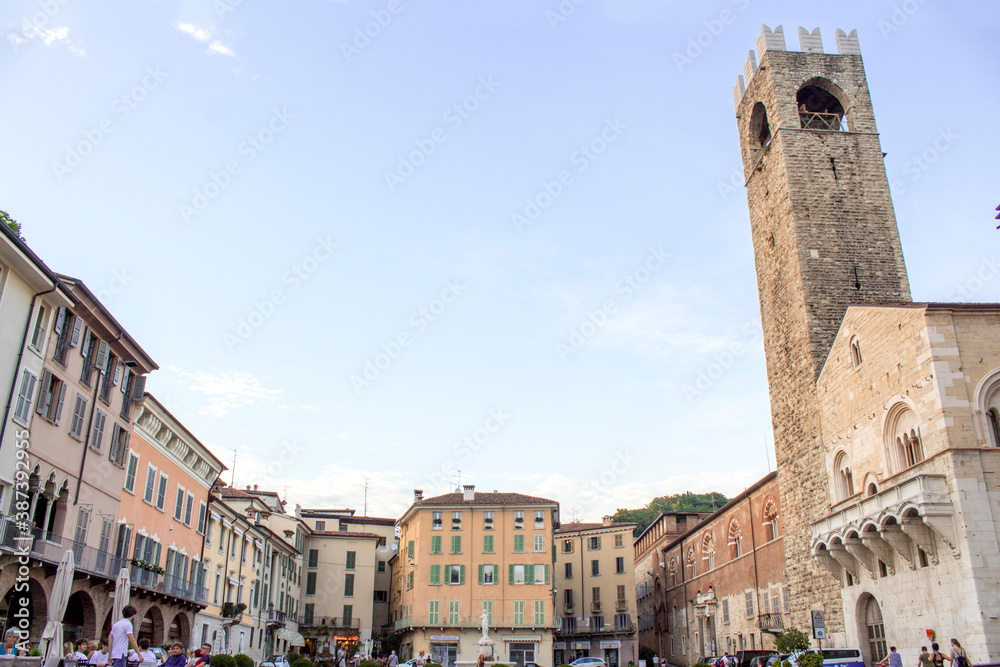 Panoramic view of Paolo VI square in Brescia, Lombardy Region - Italy. Sunset scene with clear sky, a stone church tower on the right and bricks houses around the square.