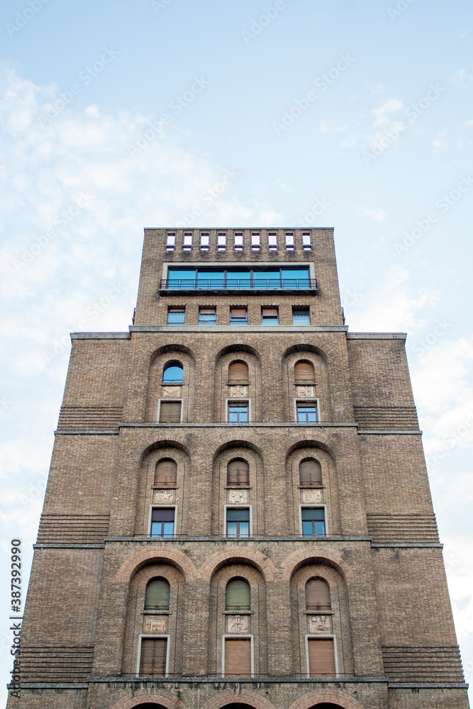 Fototapeta premium Close up soviet bricks style palace, arch windows and cloudy sky in background. Location: Brescia, lombardy region. ( Italy)