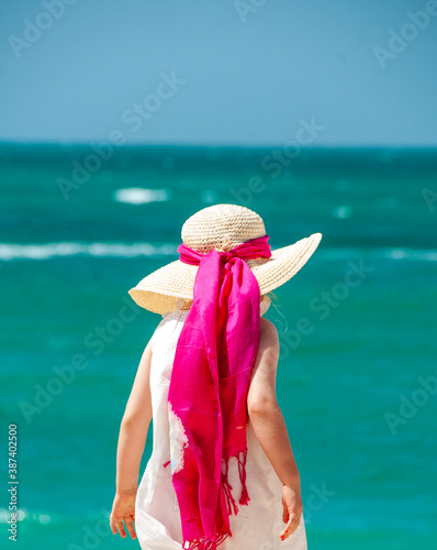 holidays at the beach with tourqouise water of the ocean in the background a girl with a hat and  a pink ribbon   photo