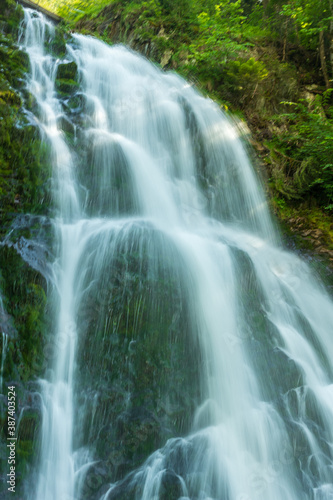 Détail d'une cascade de rivière dévalant sur des rochers foncés avec de la mousse en pose longue par une journée ensoleillée en suisse © Guillaume