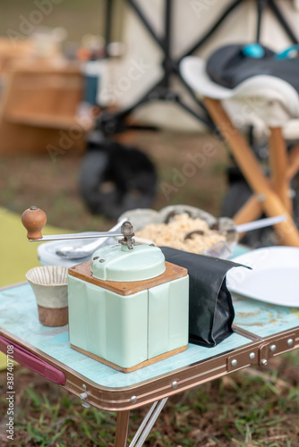 The blue cream-colored antique coffee grinder is placed near the black coffee sachets and coffee cups on a small table, camping, outdoor activities with family. And companions on vacation