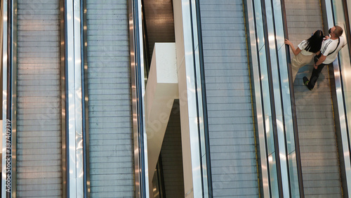 Man and a woman ride an escalator between the floors of a shopping mall. Escalator of a shopping center between levels for shoppers who go up and down, top view