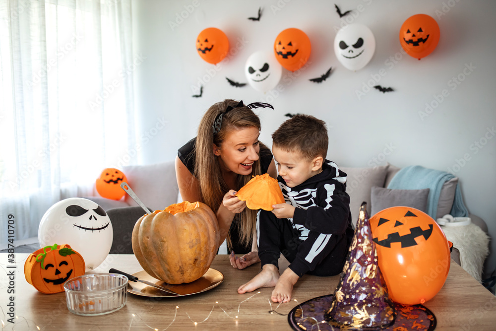 Child and mother in Halloween costume. Kids trick or treat. Face painting  for party event. Little boy dressed as skeleton with pumpkin lantern.  Family celebration. Mom and son with pumpkin. Stock Photo