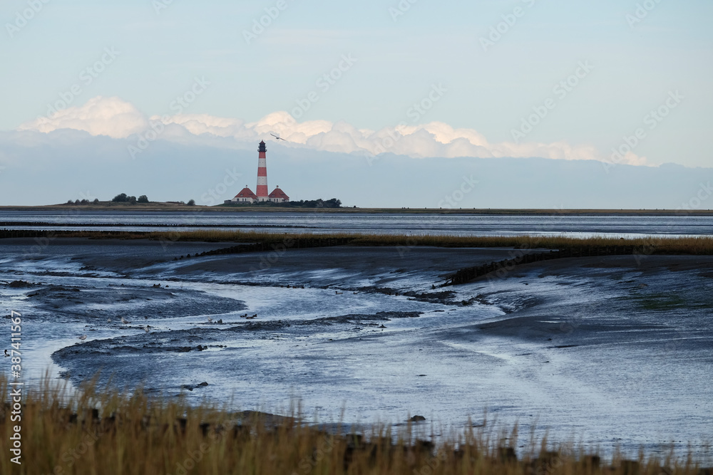Fototapeta premium Ebbe in der Nordsee mit einem Leuchtturm in Westerhever/D im Hintergrund