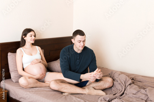 Happy pregnant family. Husband massaging his pregnant wife legs and sitting together on couch in their home photo