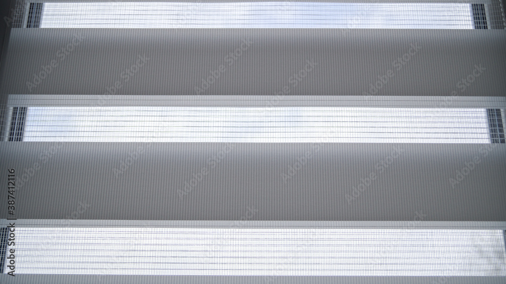 Obraz premium White roller blinds with stripes and mesh on a plastic window in the room. Day and night system. It's a nasty day. Comfort and refinement of the house.