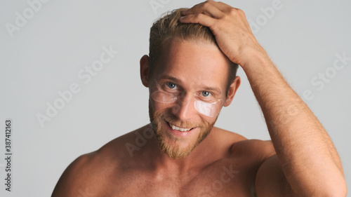 Handsome smiling bearded man applying eye patches looking happy isolated on white background