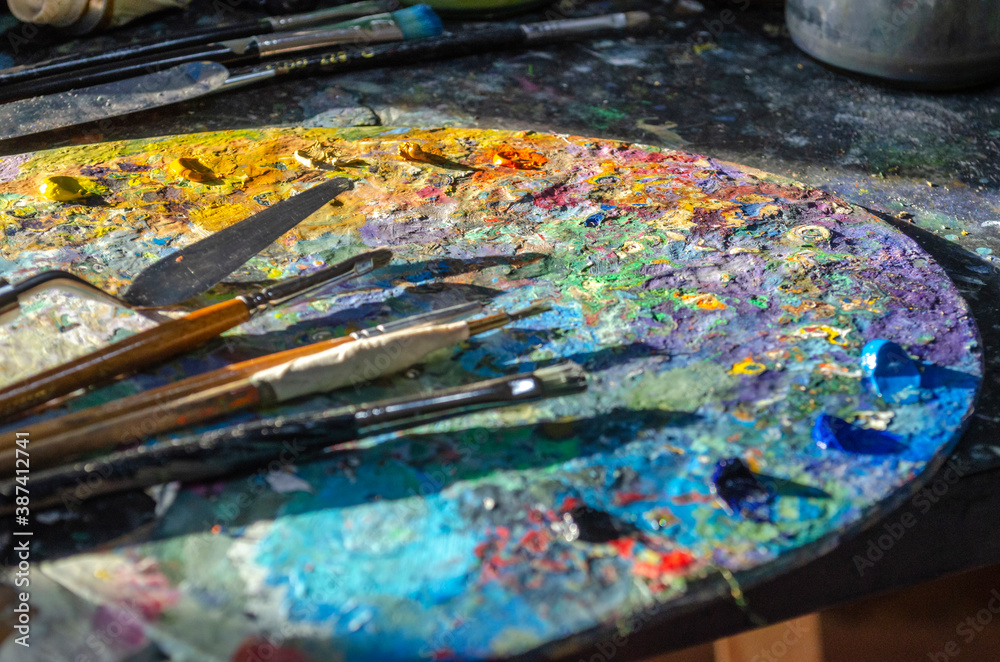 Stock Photo of a painter brushes and palette knife on a wooden palette with mixed and unmixed oil colours on sunlight. Concept art painter