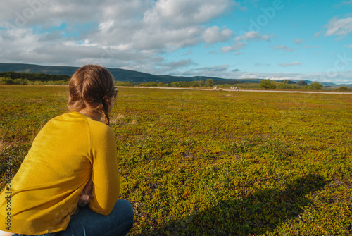 A girl watching wild reindeer family grazing on a meadow in Norway