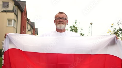 Close-up portrait of a gray-haired pensioner with glasses and a beard holding the red and white flag of Belarus. Protest in Belarus, color revolution photo