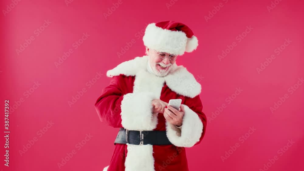 happy santa claus chatting on smartphone and touching eyeglasses isolated on red happy santa claus chatting on smartphone and touching eyeglasses isolated on red