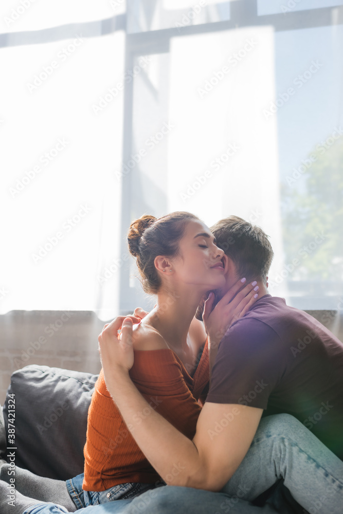 Fototapeta premium young, tender couple embracing while sitting on sofa at home