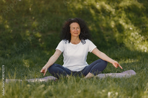 Mature lady training in a summer park. Brunette doing yoga. Old woman in a sports clothes. © prostooleh