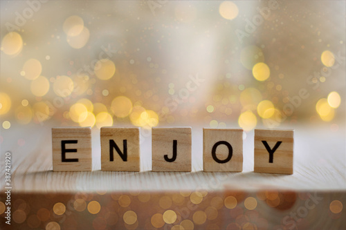 Enjoy word written on wood block on wooden table. Concepts of cozy, rest and enjoy holidays. The word ENJOY, letters on block cubes on blurred bokeh. Copy space.