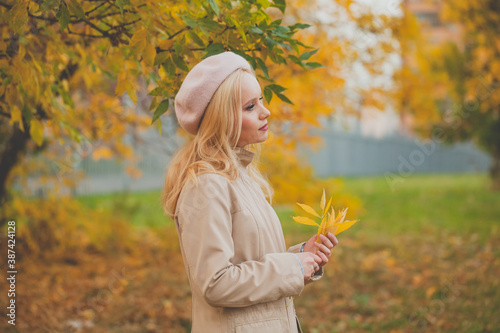 Beautiful autumn woman walking in fall park. Young model with autumn leaves in her hands on fall nature background