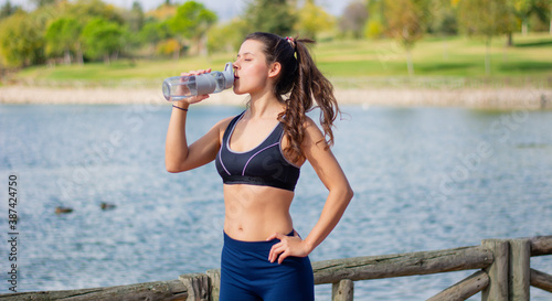 Foto de Instructor de fitness mujer delgada hermosa caucásica agua potable  durante los ejercicios de entrenamiento al aire libre. mujer en ropa  deportiva do Stock